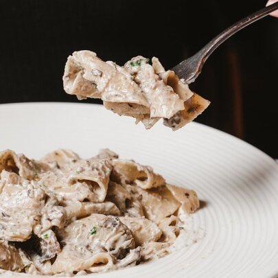A hand holding a forkful of pasta over a white bowl of pasta.
