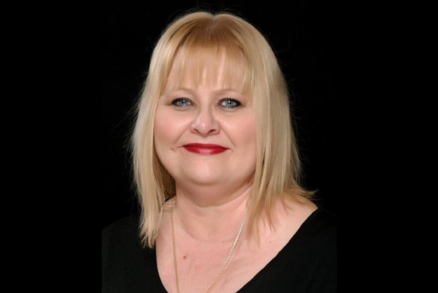 Author Vikki Petraitis with blonde hair and red lips in a black top against a black background. 