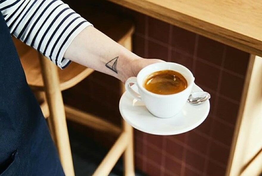 Person serving short black coffee in a small white cup and saucer.