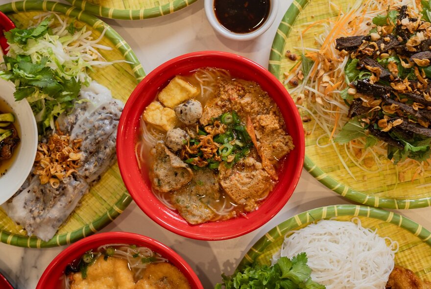 Looking down at a spread of Vietnamese dishes on woven bamboo plates.