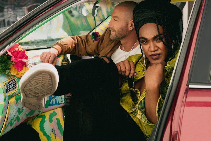 A woman and a man in a red car, the woman kicking her leg out of the open door.