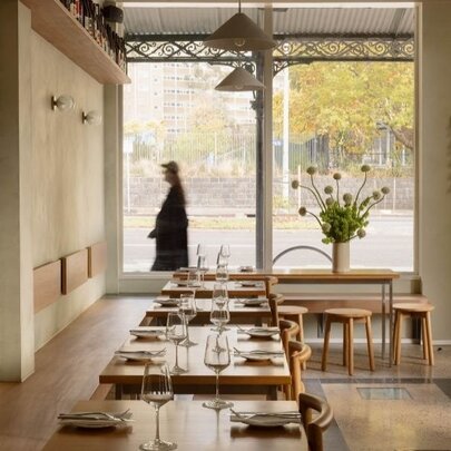 An empty neutral-toned dining space looking out the street through large windows. 