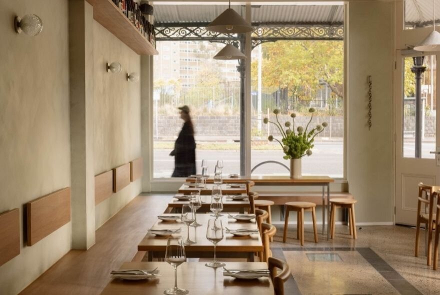 An empty neutral-toned dining space looking out the street through large windows. 