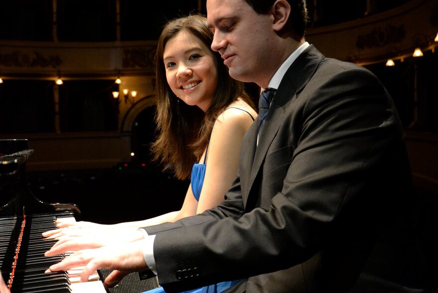 Stephanie Trick and Paolo Alderighi playing  a piano and smiling. 