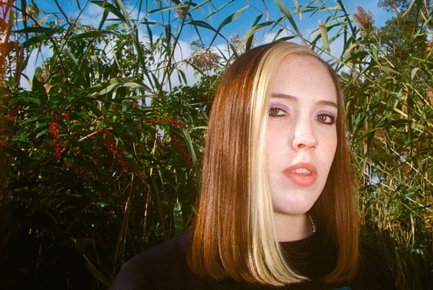 Singer, Soccer Mommy, in a field of long grasses, looking directly at the camera.