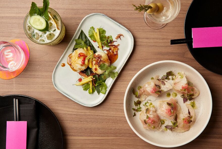 Overhead view of two plates of food on a wooden table, with eating utensils and beverages alongside.