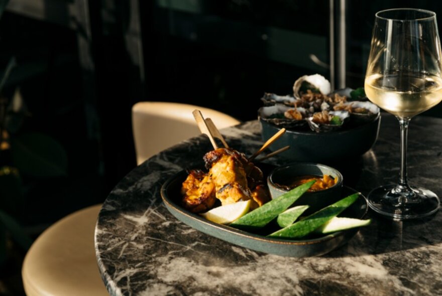 A marble table with two plates of appetisers and a glass of white wine.