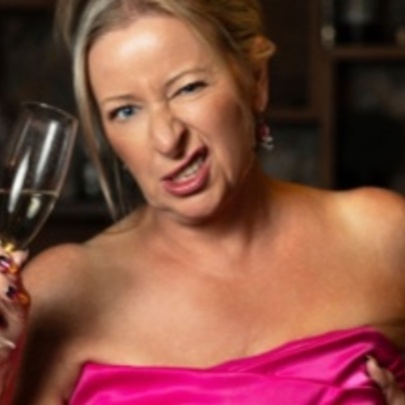 Woman wearing an off-the-shoulder pink dress, holding a glass of champagne and winking.