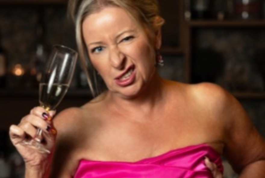 Woman wearing an off-the-shoulder pink dress, holding a glass of champagne and winking.