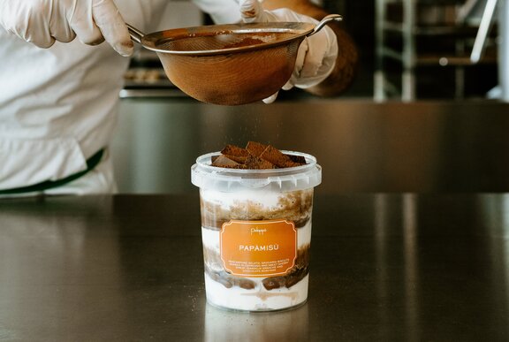 A chef dusting a tub of tiramisu with chocolate powder.