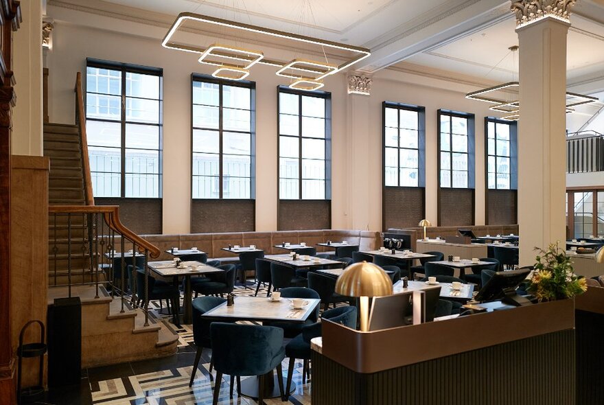The classic interior of Luci restaurant, with a staircase, and floor-ceiling-windows and dining tables and chairs.