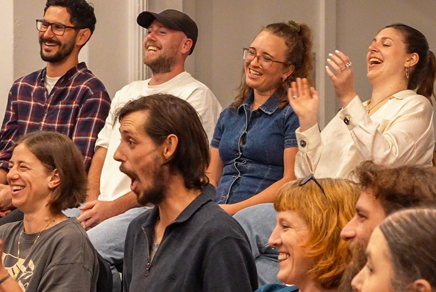 Members of an audience laughing and looking astonished while watching a magic show (out of sight).
