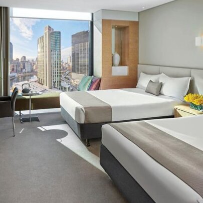Hotel room with twin beds, grey furnishings and city view.