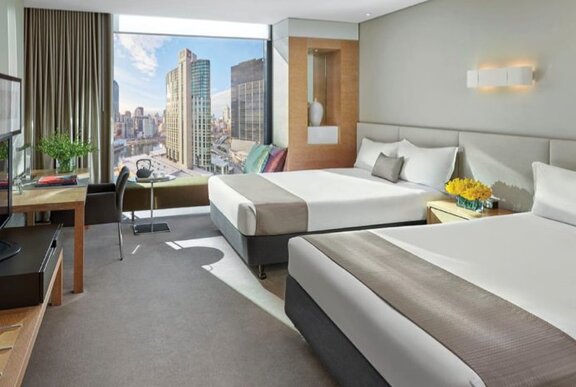Hotel room with twin beds, grey furnishings and city view.