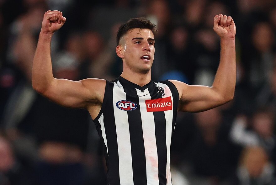Collingwood AFL football player punching both arms in the air during a match.