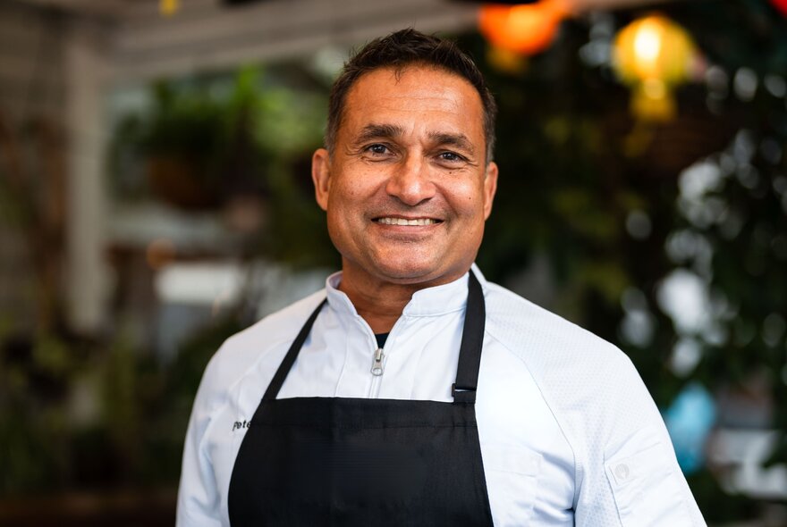Chef Peter Kuruvita smiling warmly and wearing a black apron. 