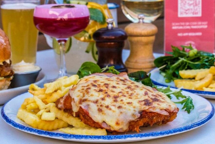 A chicken parma on a plate in front of a cocktail