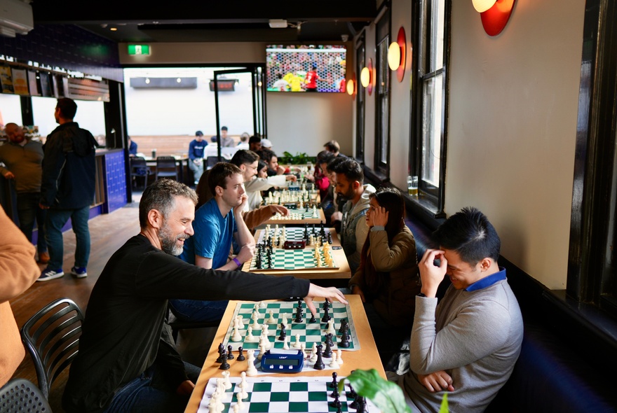 A social chess gathering where people are playing chess matches in an indoor setting of a bar.