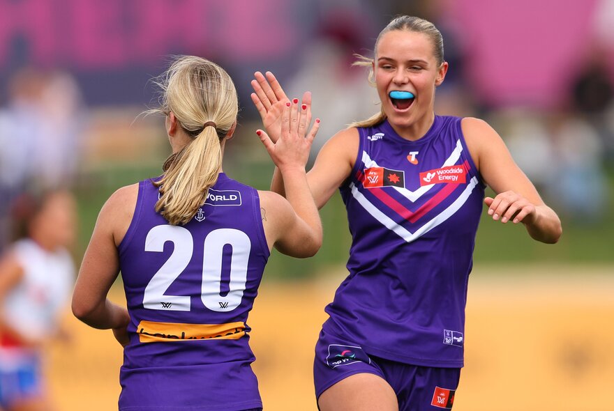 Two Fremantle AFLW players celebrating on the field, coming together for a high five.