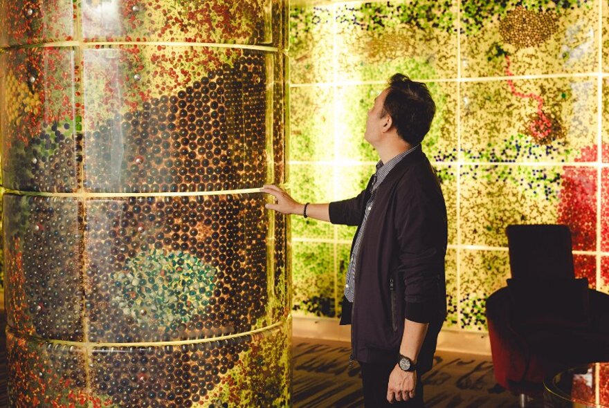 A person touching a gilded column in a room tiled with golden wall panels.