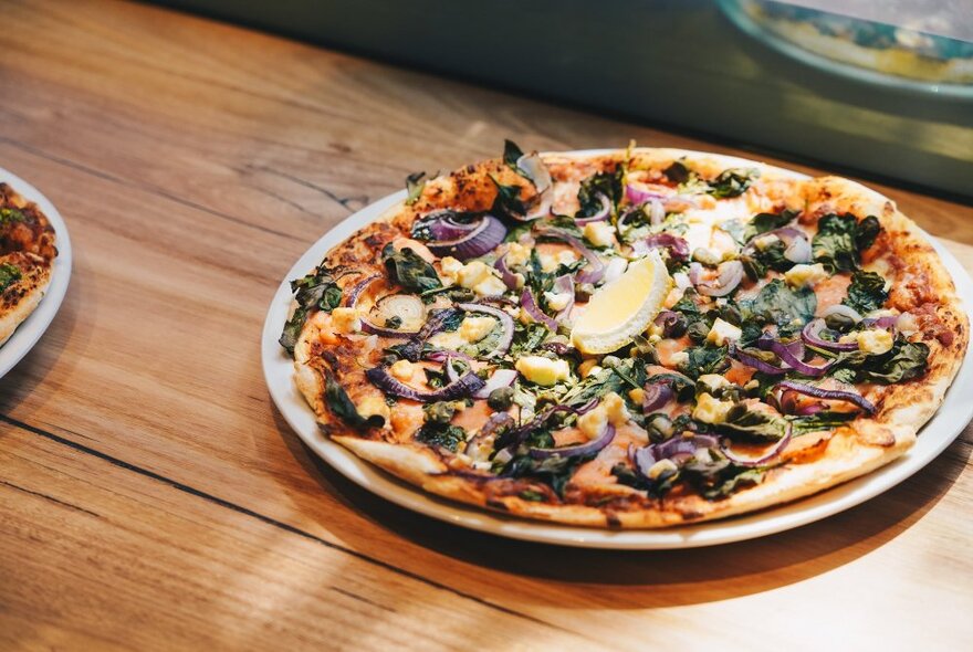 A whole pizza on a plate on top of a wooden table. 