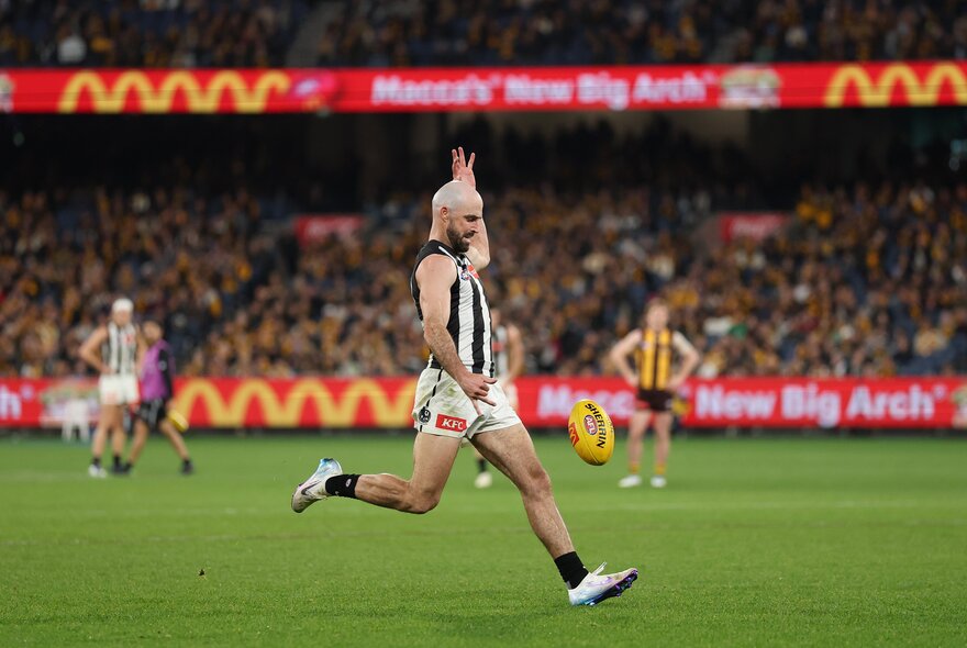 A Collingwood AFL player running on the field,  about to kick the football.