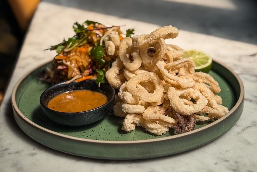 A plate of fried calamari with dipping sauce and salad, on a table at a pub.