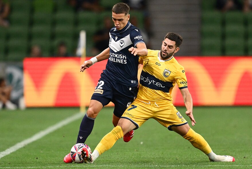 Two soccer players battle over a ball, one with his legs spit. 