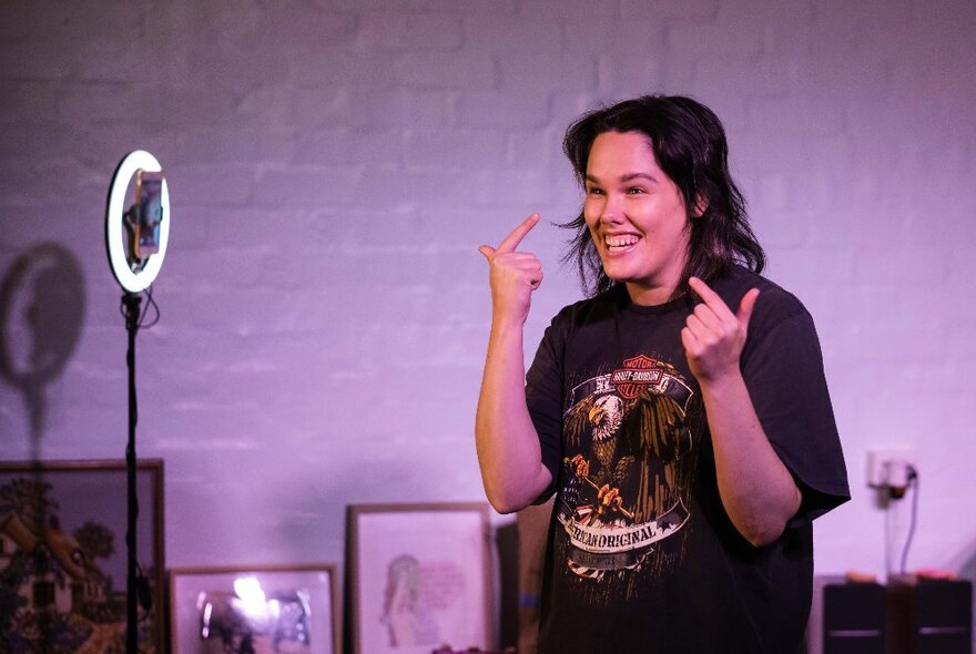 Comedian, Jenna Suffern, standing in a darkened living room gesturing at her own smile.