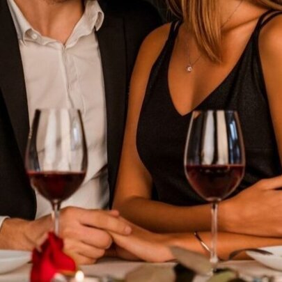 A couple holding hands and wine glasses during a candlelit dinner in a restaurant.