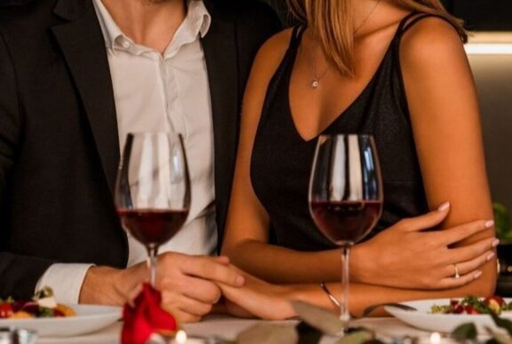 A couple holding hands and wine glasses during a candlelit dinner in a restaurant.
