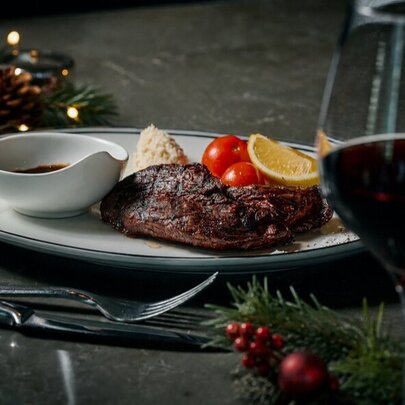 A plate of food, a glass of red wine and festive Christmas decorations on a restaurant table.