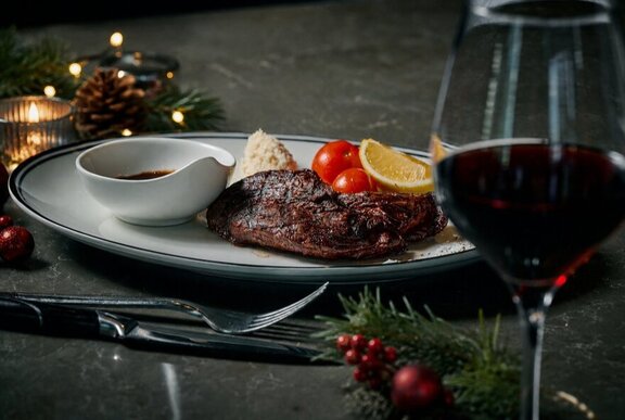 A plate of food, a glass of red wine and festive Christmas decorations on a restaurant table.