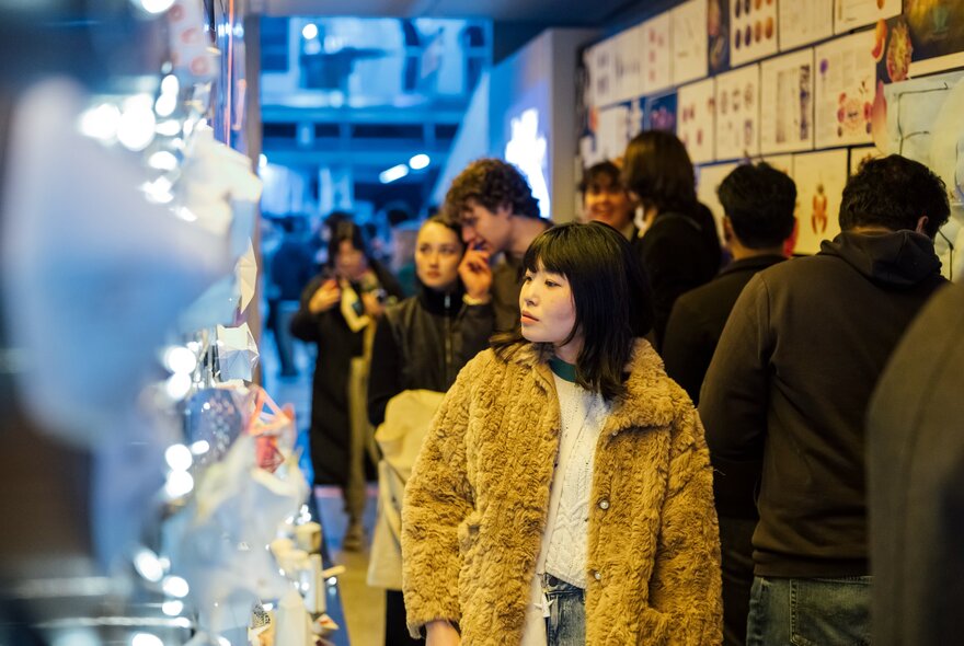 Yound adults walking through an exhibition with bright lights on one side.