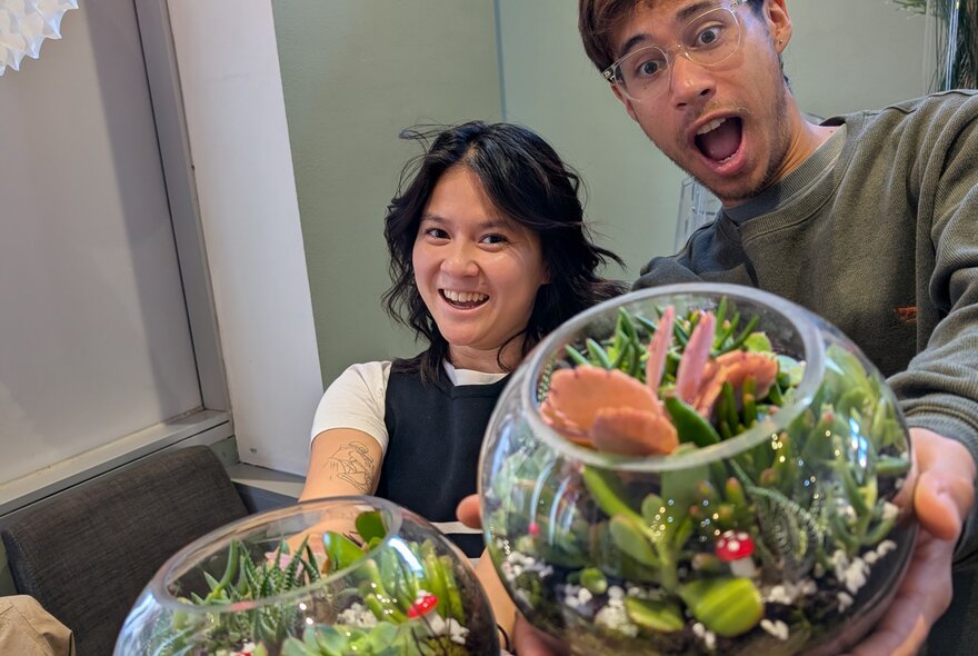 People holding their glass bowl terrariums, looking amazed.