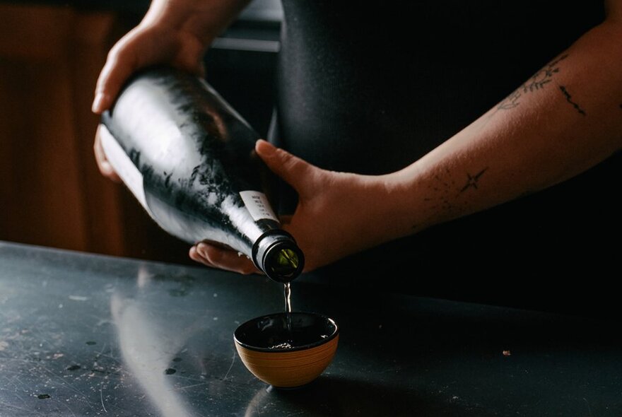 Hands pouring sake into a small bowl from a large bottle.