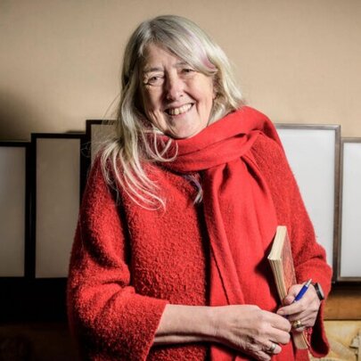Portrait of author and classicist Mary Beard, smiling as she holds a book and a pen.