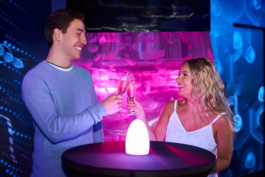 People clinking glasses in a room lit with pink and blue lights. 