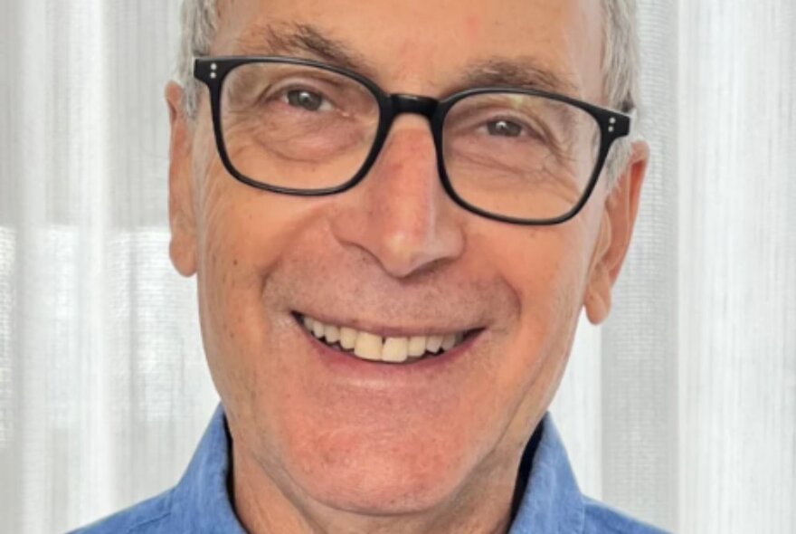 Journalist Eric Beecher, smiling wearing glasses and a blue shirt.