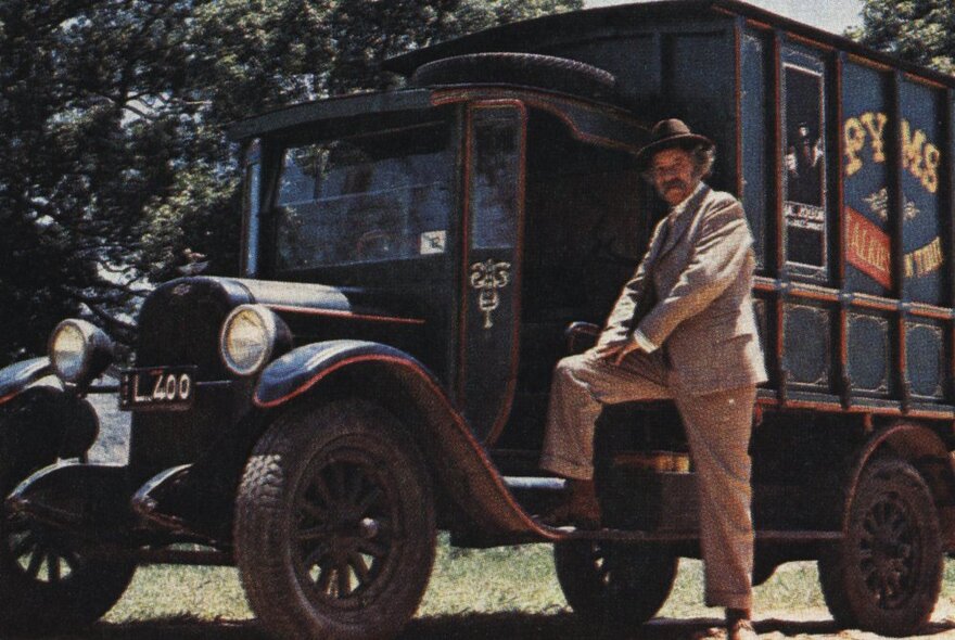 Actor John Meillon with one foot on the running board of a 1920s truck.