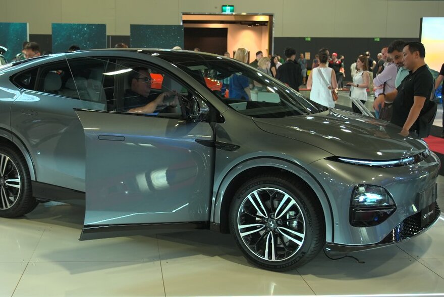 People standing next to a grey electric vehicle indoors.