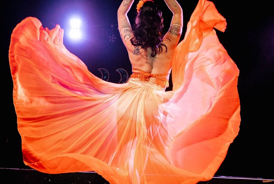 The back of a burlesque dancer with a flowing orange dress behind her. 