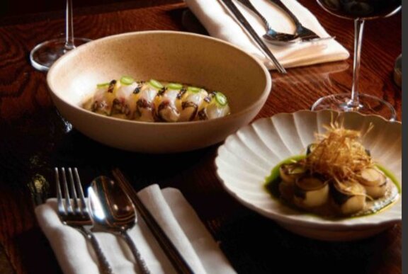 Moodily lit restaurant table with dishes of seafood, cutlery and wine glass.