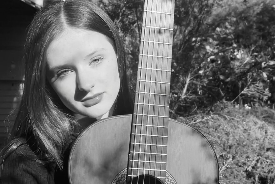 Black and white portrait of Australian classical guitarist, Ruby Cheyne, and her acoustic guitar.