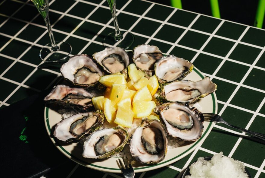 A plate of oysters with lemon slices on a black-tiled surface.