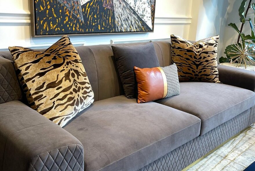 Comfortable looking grey couch, with four loose cushions on it, and a ornament on a side table next to it, on display in a shop.