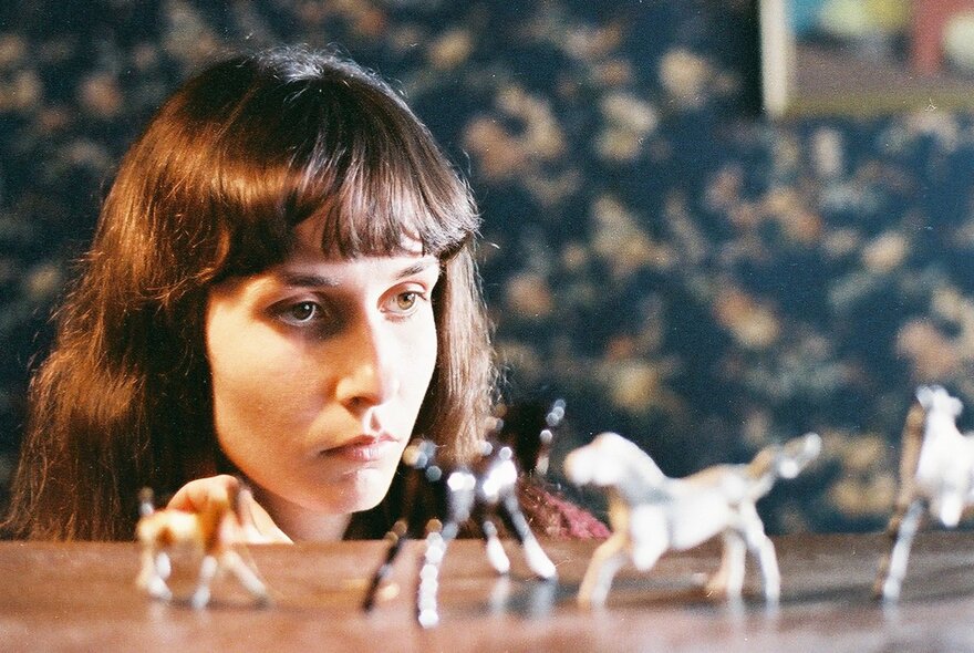 A still from a film showing a young woman looking closely at small toy animals.