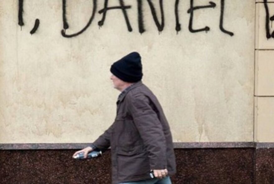 Person walking past a graffitied wall, wearing a winter coat and hat.