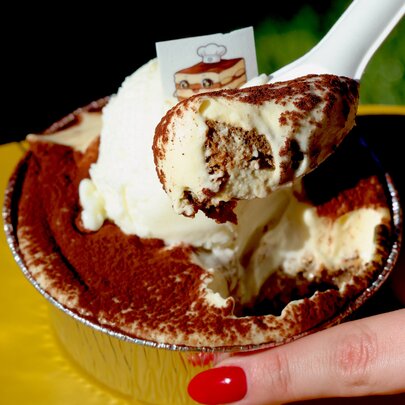A spoonful of tiramisu dessert being scooped out of a cup.