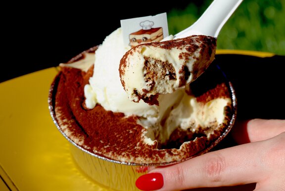 A spoonful of tiramisu dessert being scooped out of a cup.